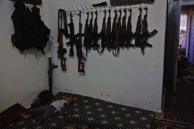 A child sleeps under the weapons stored in a FSA neighborhood headquarters in the countryside of Idlib, Syria. Photo by Rachel Beth Anderson.