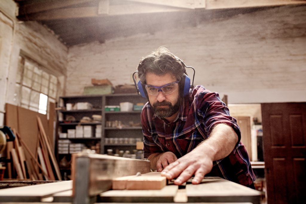 Carpentry business owner cutting a plank of wood in workshop