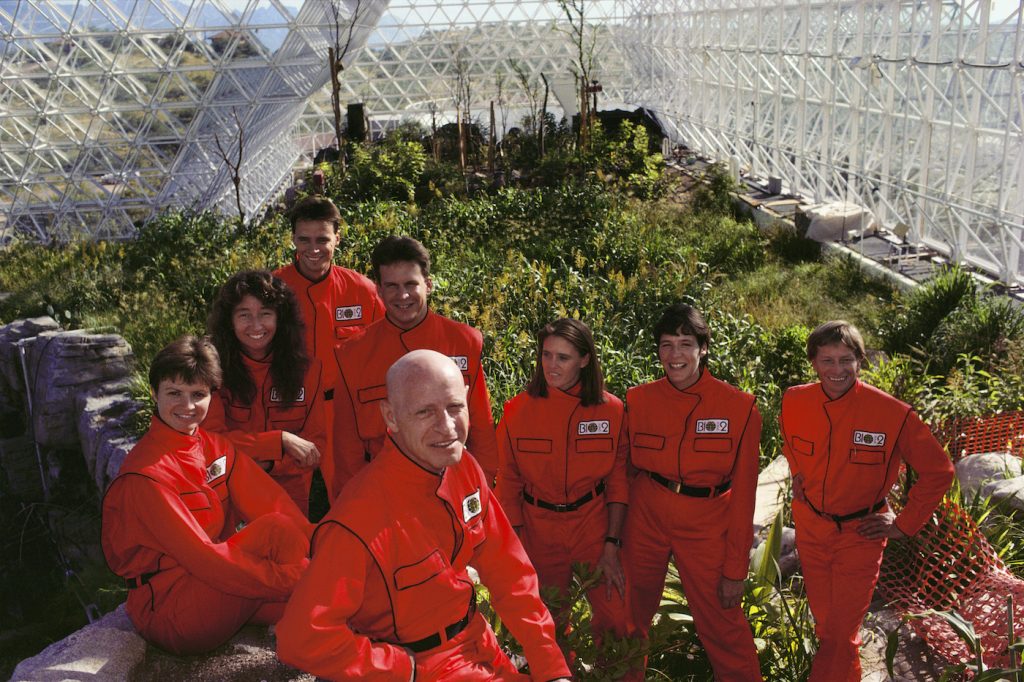 Biosphere 2 Project undertaken by Space Biosphere Ventures, a private ecological research firm funded by Edward P. Bass of Texas. Candidates for (1990)’s Biosphere 2 project. Dr. Roy Walford (bald) is front and center. Biosphere 2 was a privately funded experiment, designed to investigate the way in which humans interact with a small self-sufficient ecological environment, and to look at possibilities for future planetary colonization. The $30 million Biosphere covers 2.5 acres near Tucson, Arizona, and was entirely self- contained. The eight ‘Biospherian’s’ shared their air- and water-tight world with 3,800 species of plant and animal life during their two-year isolation experiment. The project had problems with oxygen levels and food supply, and has been criticized over its scientific validity.(1989)