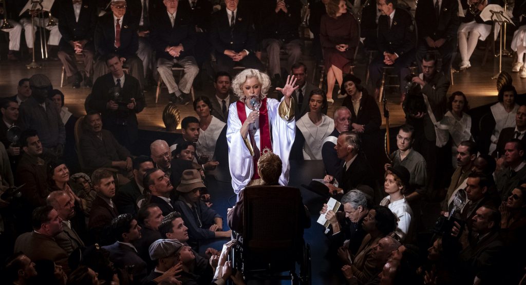 Sister Alice (Tatiana Maslany) works a miracle inside the Radiant Assembly of God interior, at the historic Trinity Auditorium location in downtown L.A. The four day shoot in September 2019 utilized more than 400 background actors each day, including a mass of congregants. Background cast with special improvisational skills were placed close to Maslany, near the stage, to be visible to camera as they portrayed being “saved,” speaking in tongues and other activity. Courtesy HBO.