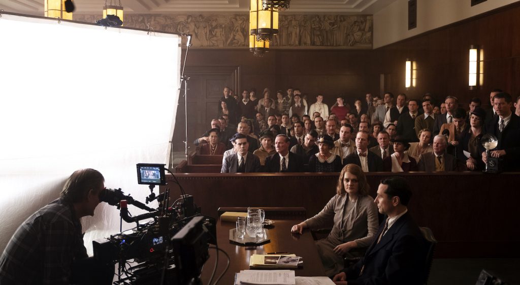 Camera operator Don Devine lines up a shot of Matthew Rhys (Perry Mason) and Gayle Rankin (Emily Dodson) in the Courtroom set on Paramount Stage 27, as background cast performs behind them.  The best background are ones audiences don’t even notice, Mollie Stallman notes. Photo by Merrick Morton/HBO.