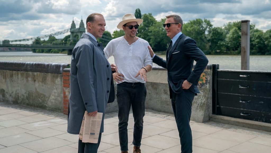 Ralph Fiennes (M), director Cary Joji Fukunaga and Daniel Craig (James Bond) on the set of NO TIME TO DIE, an EON Productions and Metro-Goldwyn-Mayer Studios film Credit: Nicola Dove © 2021 DANJAQ, LLC AND MGM. ALL RIGHTS RESERVED.