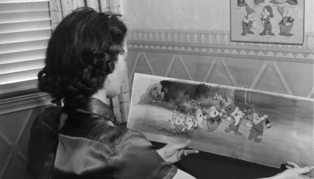 A black and white still depicting an Ink & Paint artist holding a painting of the Seven Dwarfs for Walt Disney’s animated feature Snow White and the Seven Dwarfs. Courtesy Walt Disney Archives, Photo Library.